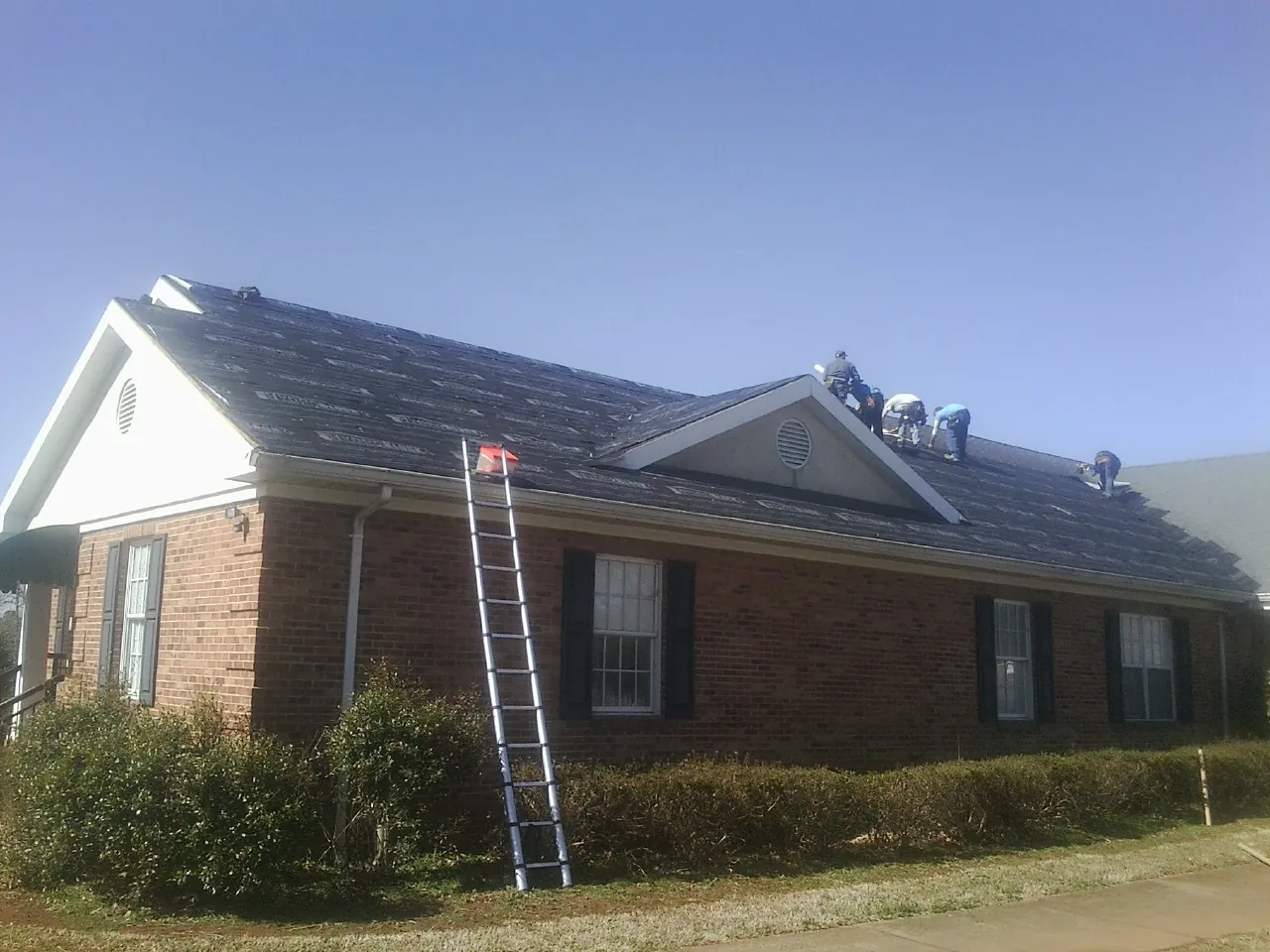 Crew tearing shingles off a brick ranch roof with a ladder set — Emergency Roof Repair work by our crew in Strabane
