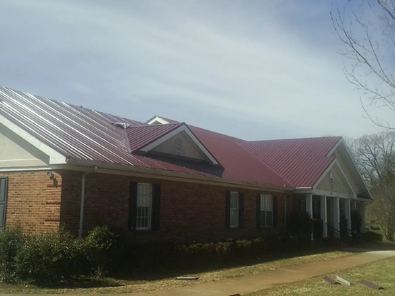 Red metal roof with gabled entries on a long brick building, from a Hail Damage Roof Repair job in Strabane