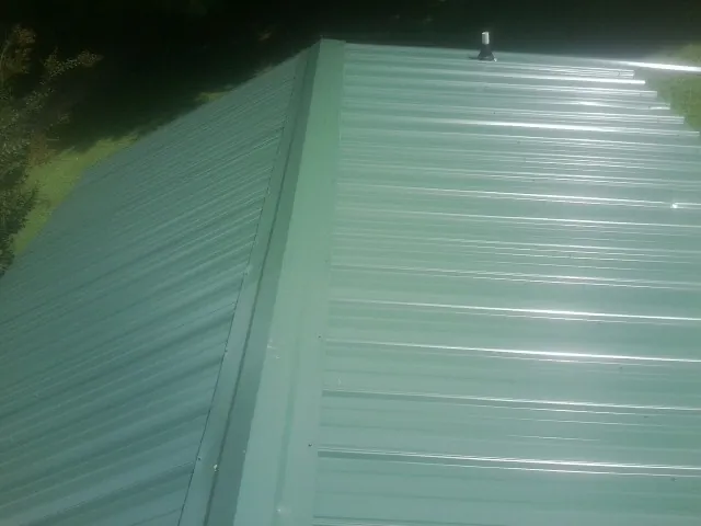 New green metal panels meeting at the ridge of a roof — Flat Roof Repair work by our crew in Strabane