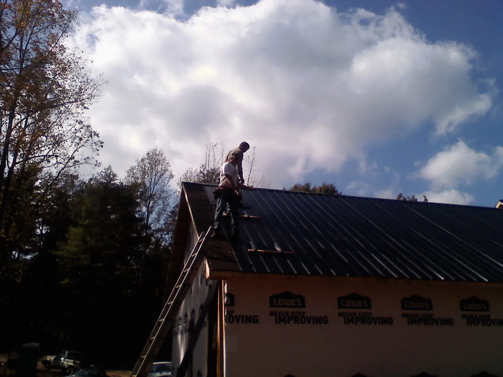 Roofer fastening dark metal panels high against a cloudy sky, from a Roof Inspection job in Strabane