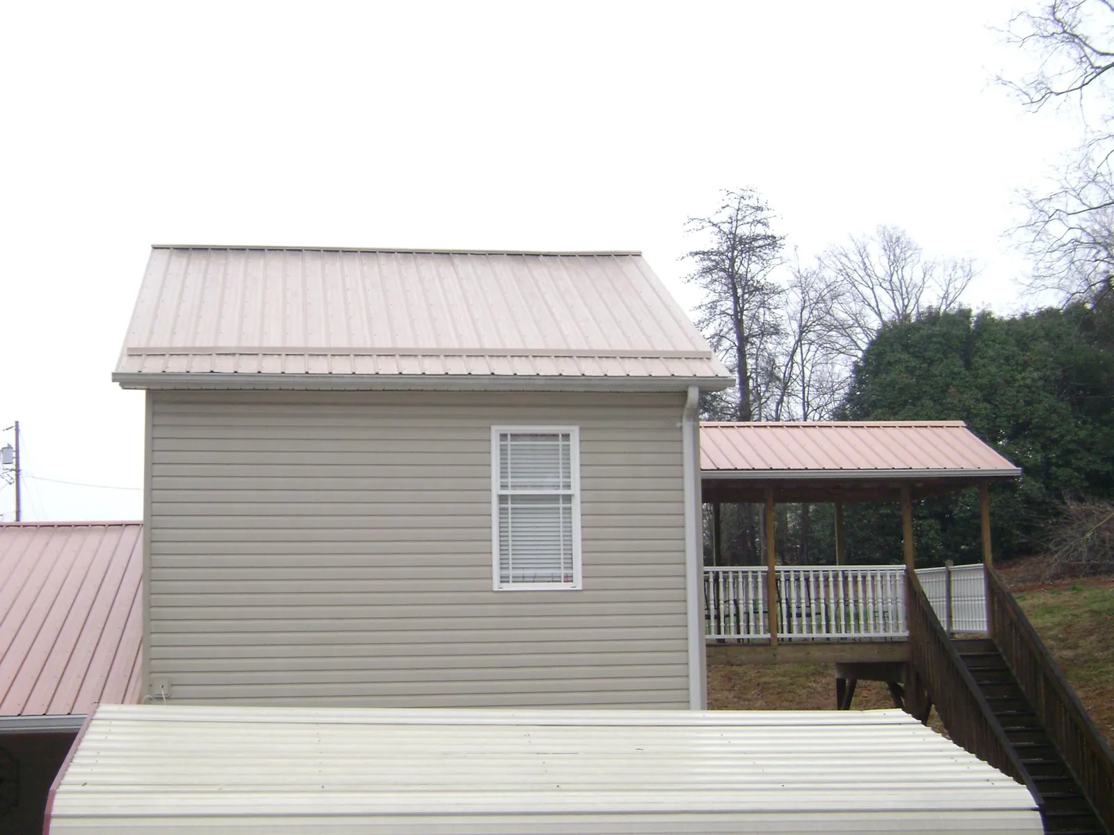 Tan metal roofs on a two story addition and attached porch, from a Roof Replacement job in Strabane